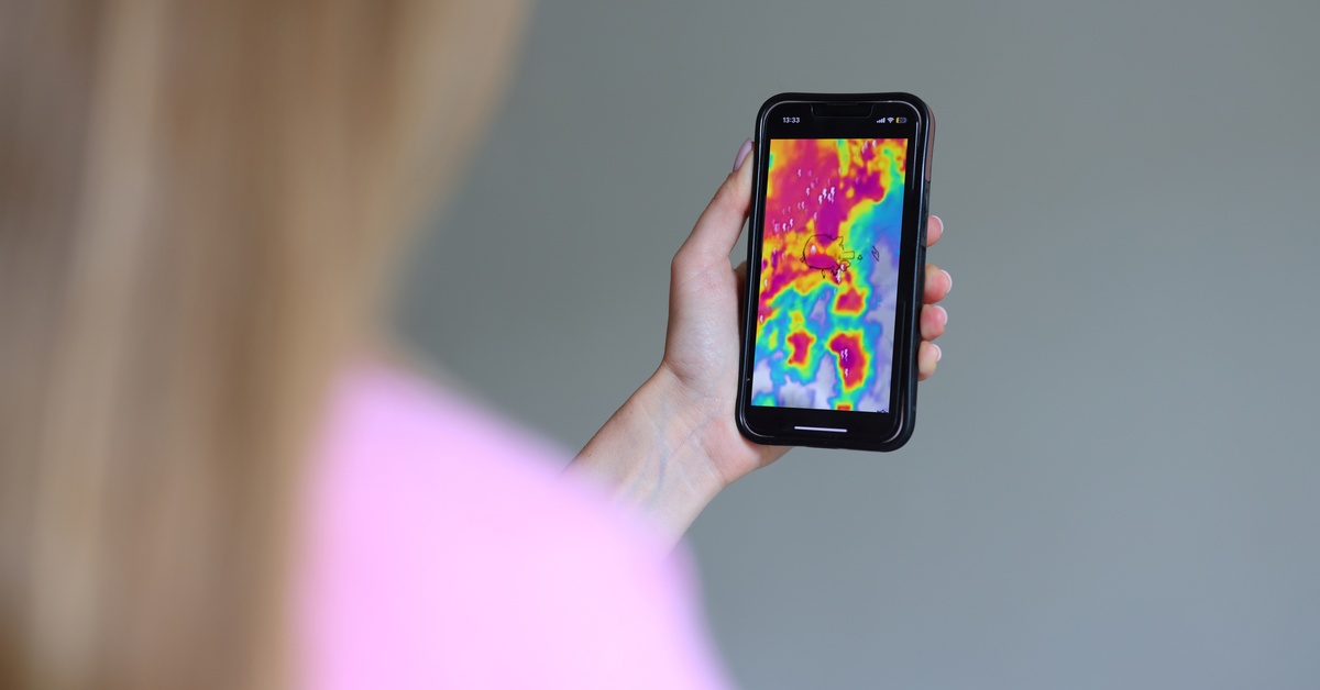 A woman checking the weather radar on her phone. There is a lot of red in the section she's looking at.